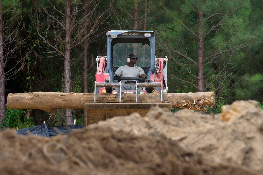 An airman operates a skid steer to transport a log for burning.