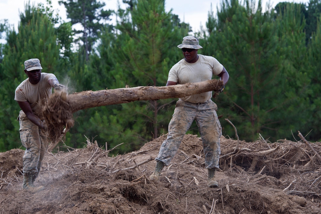 Airmen toss a large piece of wood into a pile.