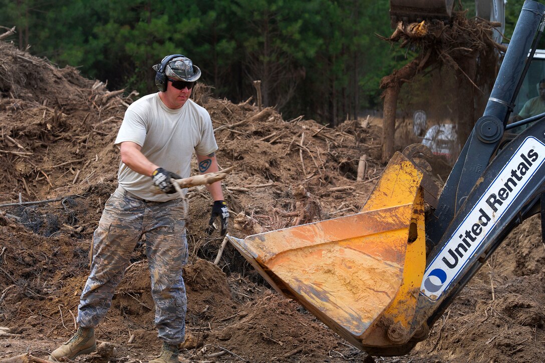 An airman tosses wood into a bucket on a backhoe.