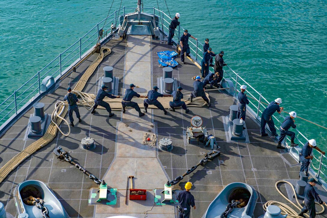 Sailors pull a line on the deck of a ship.