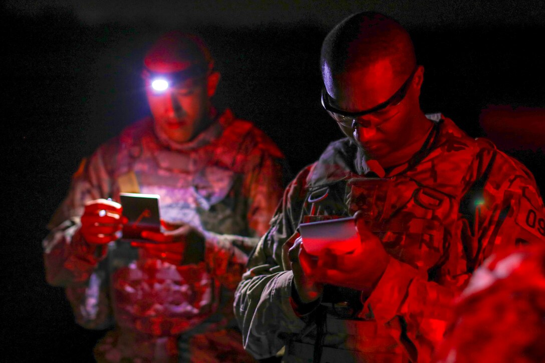 Two soldiers look at notepads at night.