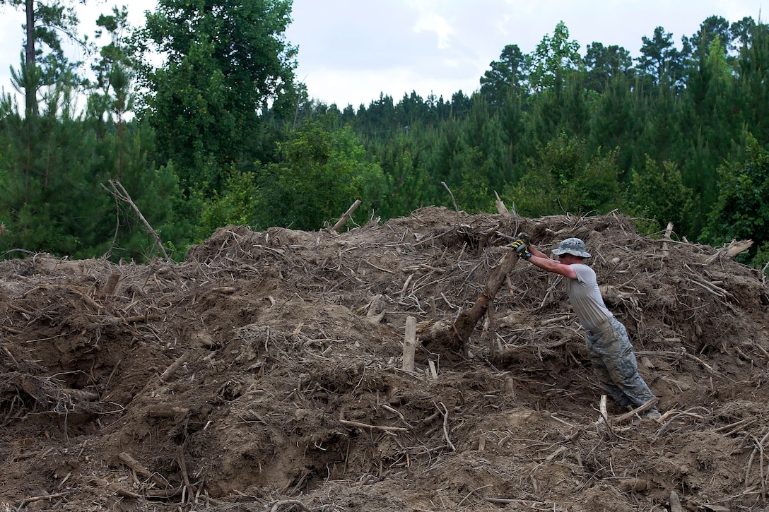 An airman lifts wood from a pile.