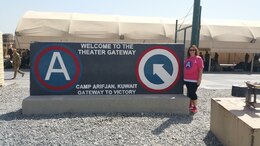 Theresa Scott, family readiness support assistant, 1st Theater Sustainment Command (TSC), stands in front of the 1st TSC Theater Gateway T-Wall, June 18. Scott traveled to Camp Arifjan to experience life as a Soldier on deployment.