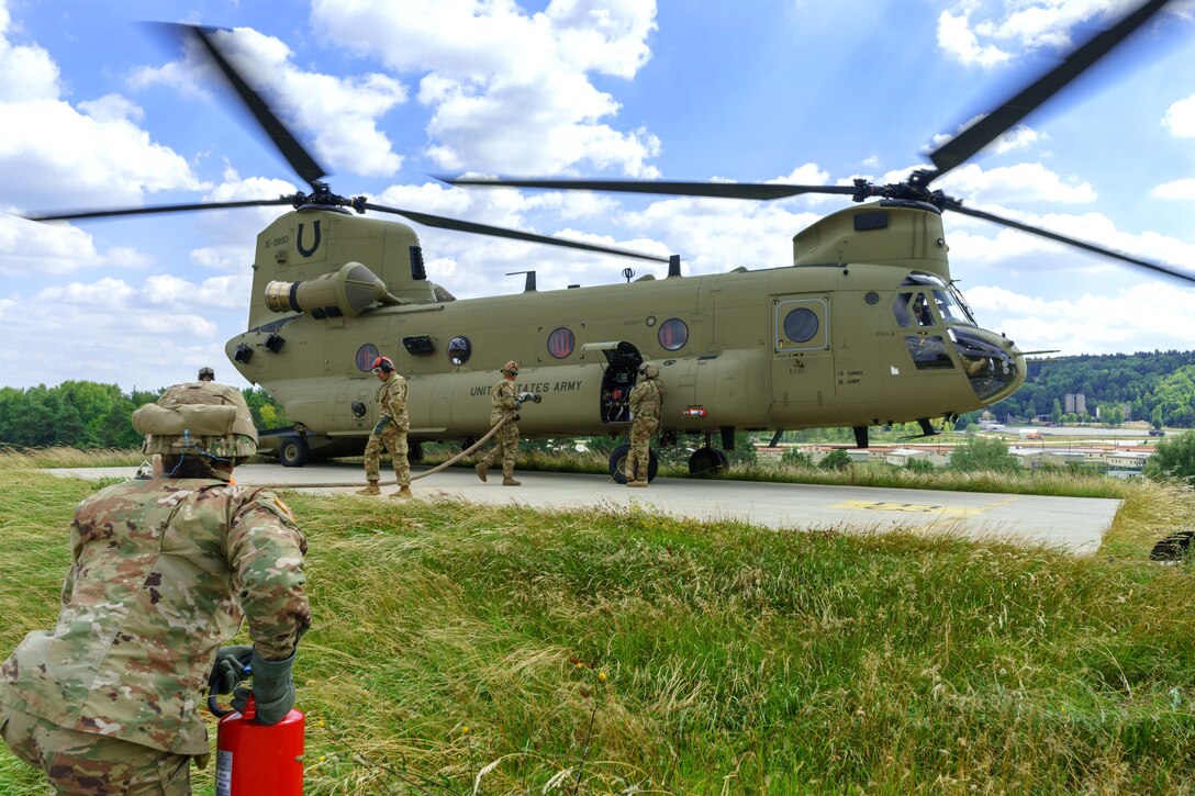 A soldier stands watch with fire extinguisher while others refuel a helicopter.