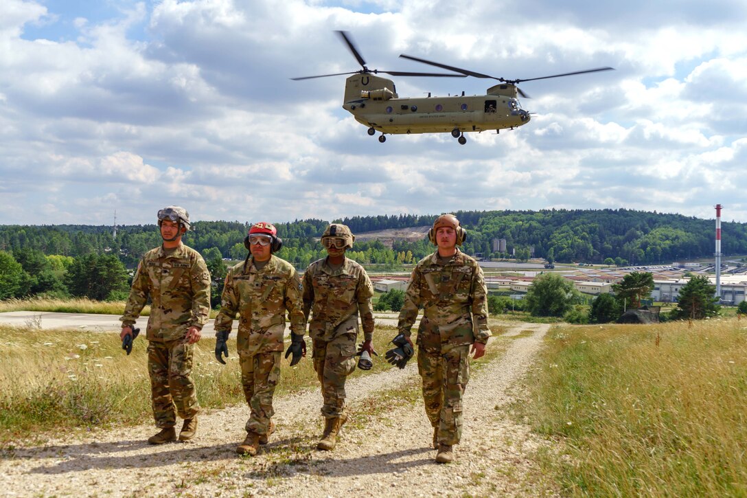 Soldiers walk down a gravel road as a CH-47 Chinook helicopter takes off.