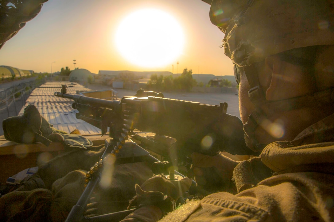 A Marine holds a weapon with the sun in the background.