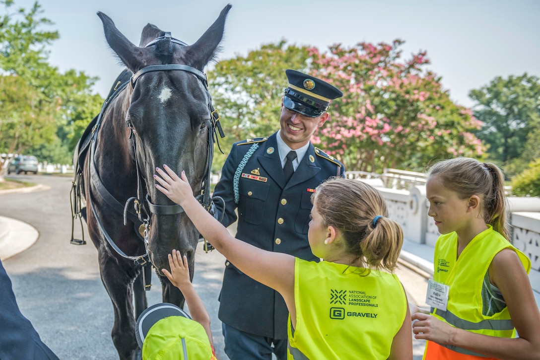 Children pet a horse as a soldier holds the reins.