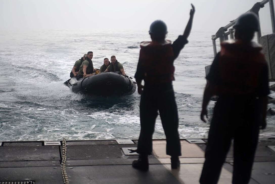 Sailors stand on the stern gate of an amphibious dock landing ship.