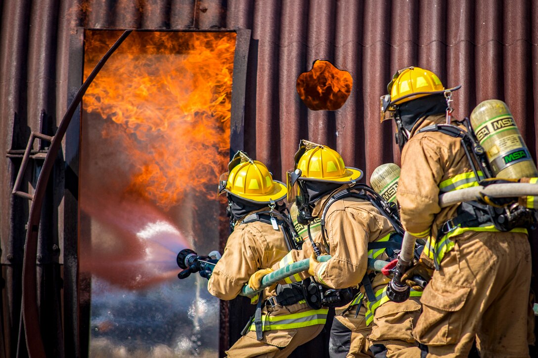 Three firefighters hold spray a fire with a firehose.