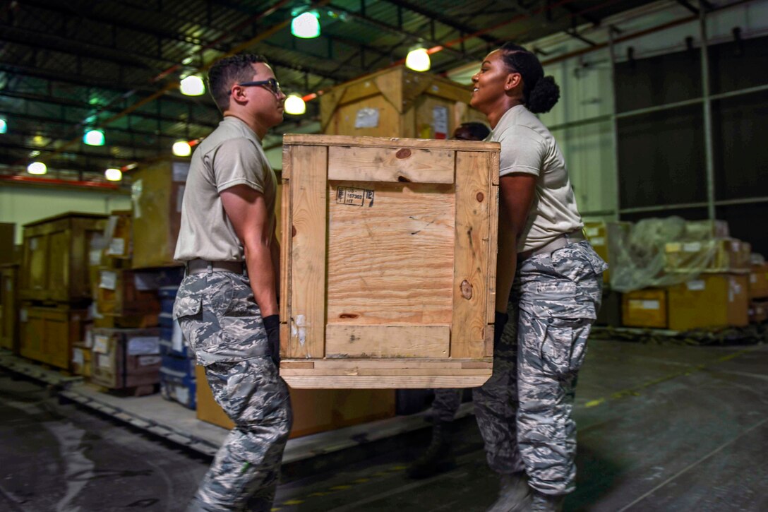 Two airmen carry a box.