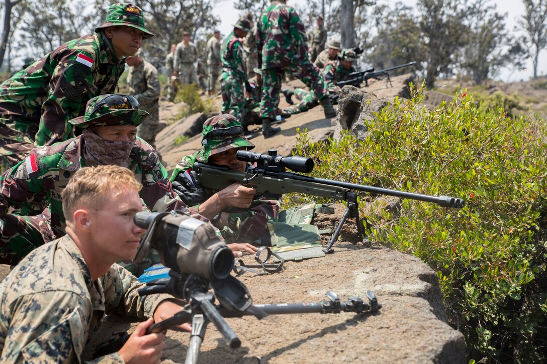 Indonesian Marine Sgt. Dedy, right, a sniper with the Indonesian Marine Corps, looks through his scope down range while U.S. Marine Cpl. Benjamin Garcia, a joint fires observer with scout sniper platoon, 1st Battalion, 3rd Marine Regiment, observes the shot groupings during live-fire training as part of Rim of the Pacific (RIMPAC) exercise at Pohakuloa Training Area, Hawaii, July 14, 2018. The live-fire training integrated sniper teams from other RIMPAC participants with U.S. Marines, which provides high-value training for task-organized, highly capable Marine Air-Ground Task Force and enhances the critical crisis response capability of U.S. Marines in the Pacific.