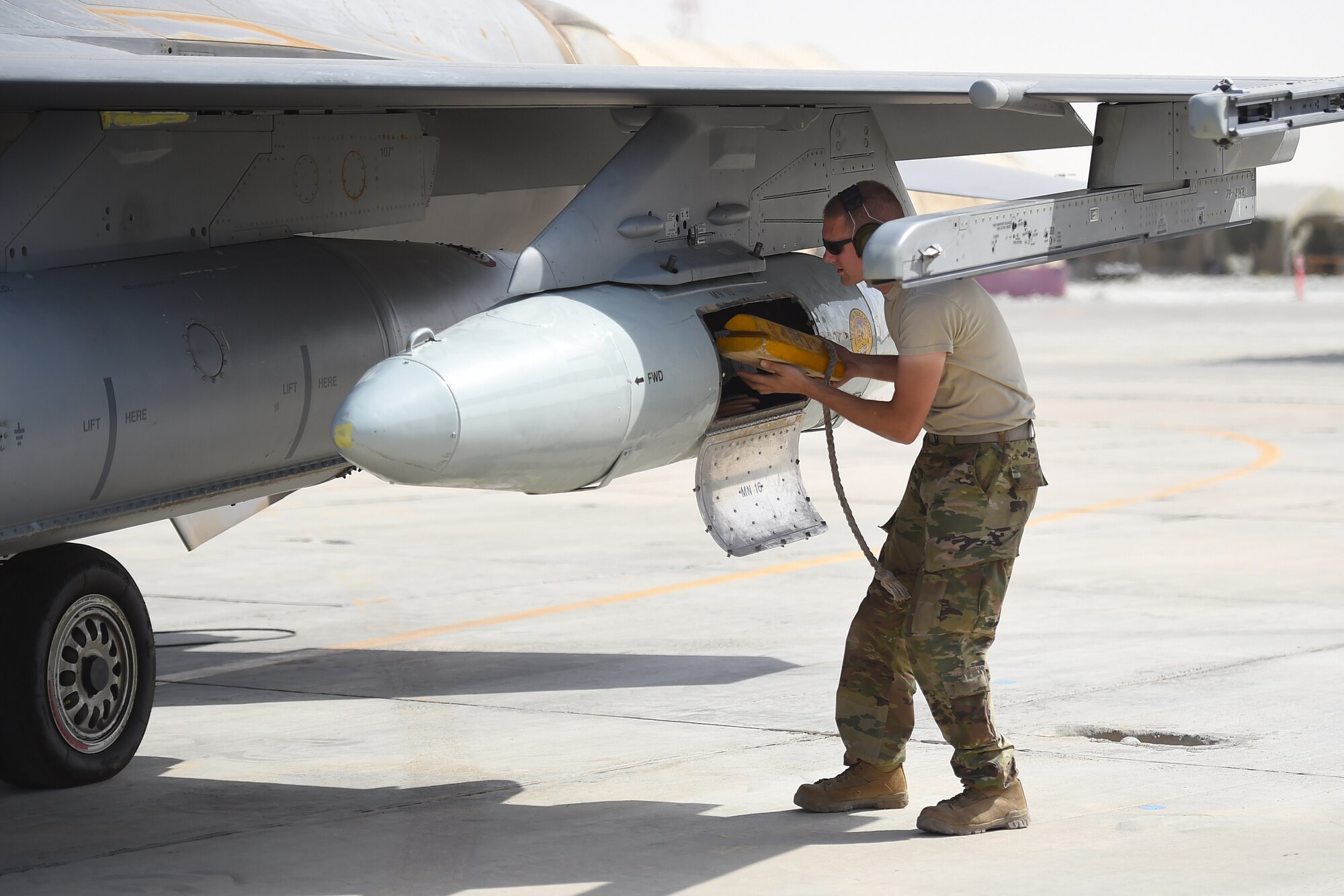 An Airman puts wood blocks into a travel pod of an F-16 fighter jet