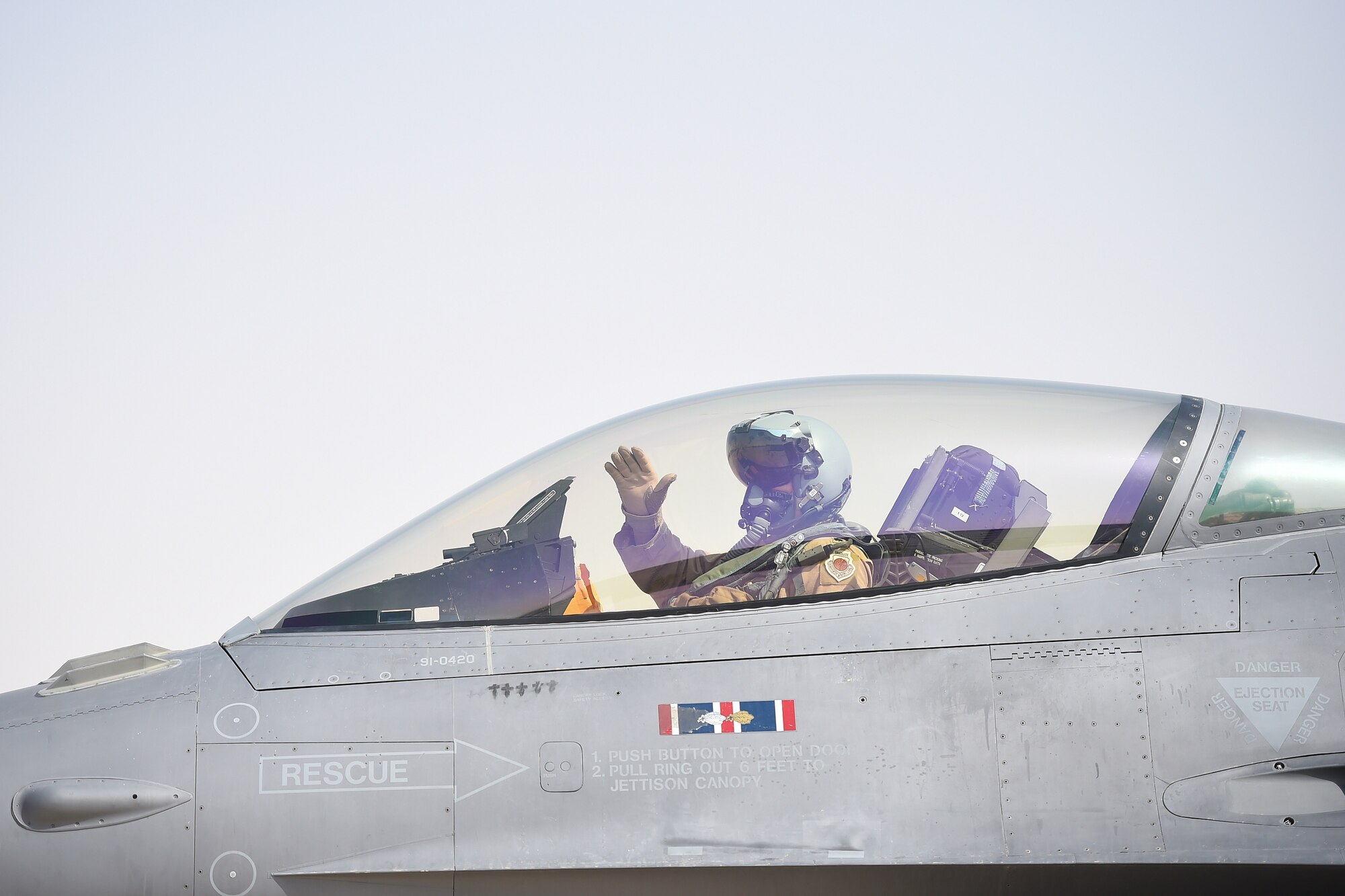 A pilot waves goodbye from inside the cockpit of an F-16