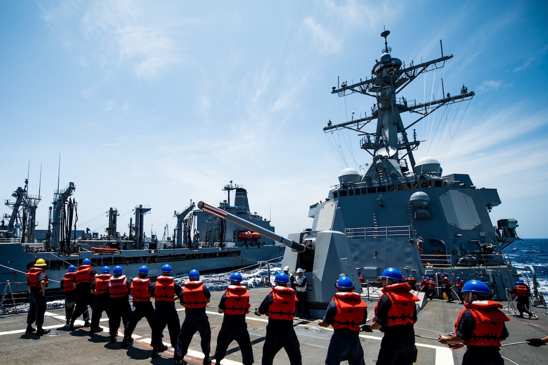 A group of sailors hold onto a line aboard a ship.