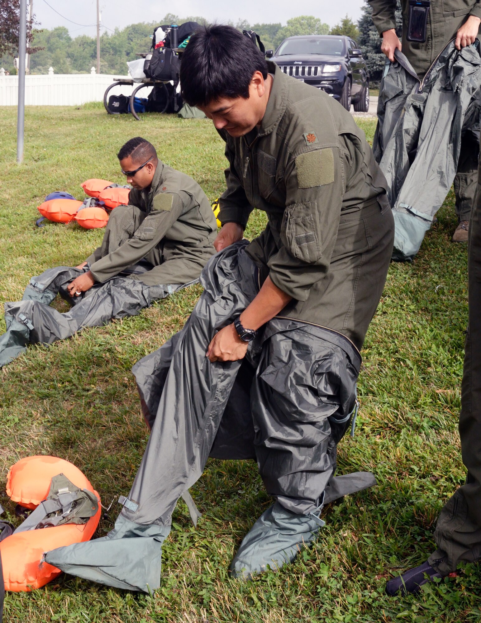 Maj. Chris Lamkey (standing) and Maj. Clay Holland (sitting), 170th Group members assigned to Offutt Air Force Base, Nebraska, don anti-exposure suits while participating in water survival and rescue training July 14, 2018. The suits are worn by aircrew in the eventuality they must be in water where the temperature is below 60 F. The air crew members were briefed on the availability and use of tools contained in their survival gear before putting academics and theory to the test in the waters of a local lake.