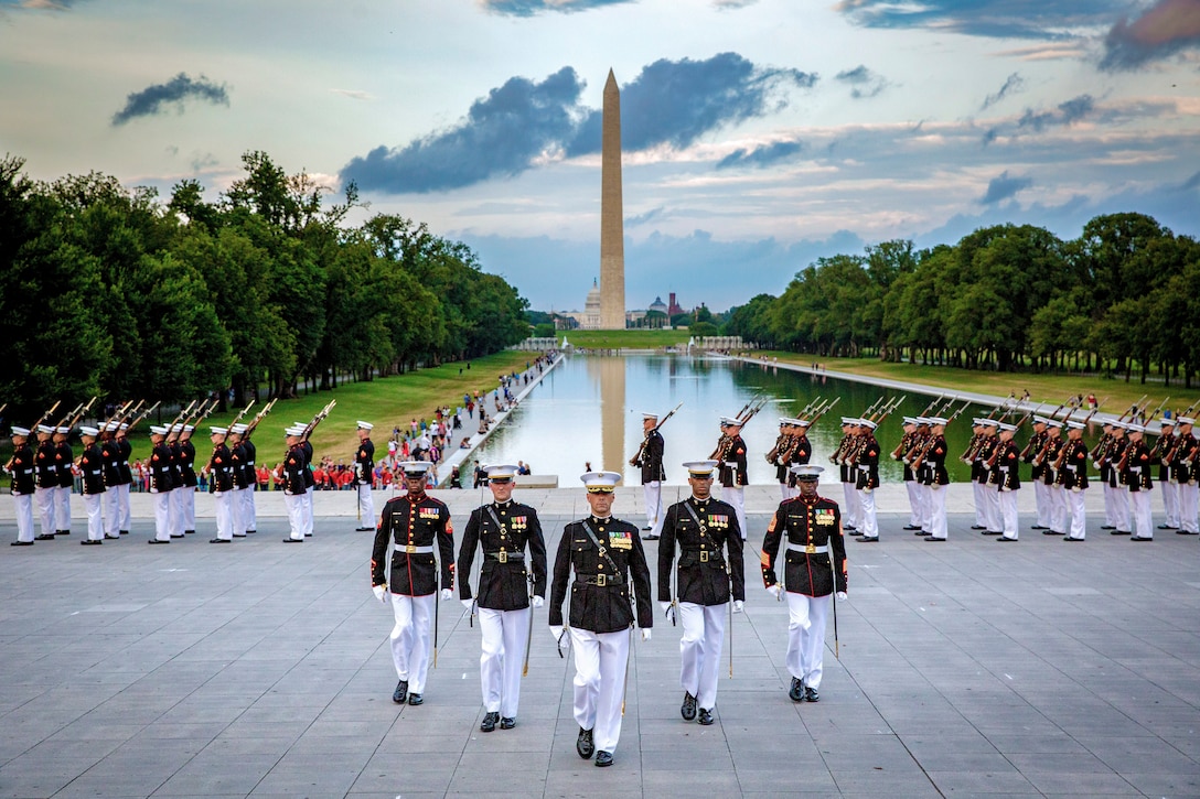 Marines march in front of the reflecting pool with the Washington Monument in the background.