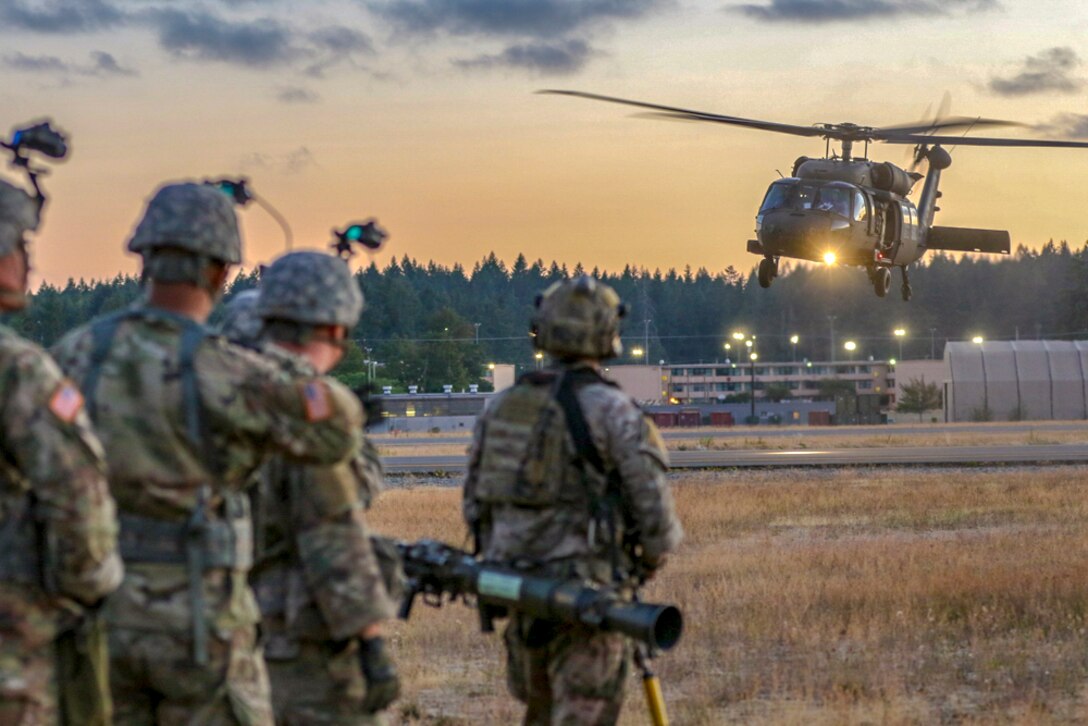A helicopter lands in the background with soldiers waiting.
