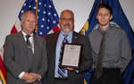 IMAGE: DAHLGREN, Va. (July 19, 2018) - John Fiore, Naval Surface Warfare Center Dahlgren Division (NSWCDD) technical director, holds a plaque reproduction of the patent certificate he presented to Gerhard Thielman and his son, Benjamin, at the NSWCDD Patent Awards ceremony. The father and son team were among 32 patent holders honored before family, friends and colleagues at the NSWCDD Patent Awards ceremony. "The potential benefit to the warfighter is an adaptable, self-contained vehicle with multi-mission capability," said NSWCDD Chief of Staff Chuck Campbell regarding the Thielmans' innovation.  (U.S. Navy photo by Ryan DeShazo/Released)