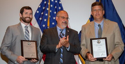 IMAGE: DAHLGREN, Va. (July 19, 2018) - John Fiore, Naval Surface Warfare Center Dahlgren Division (NSWCDD) technical director, claps after presenting a plaque reproduction of a patent certificate to NSWCDD inventors - Stephen Dix and Tracy White, left to right. They were among 32 patent holders honored before family, friends and colleagues at the NSWCDD Patent Awards ceremony. Dix and White were recognized for their patented innovation, ' Tripod mount with a Traverse Support Mechanism'. This invention is a durable weapons tripod that is easily stowed and deployed. The warfighter is provided with a reliable tripod mount that reduces logistics concerns. (U.S. Navy photo by Ryan DeShazo/Released)