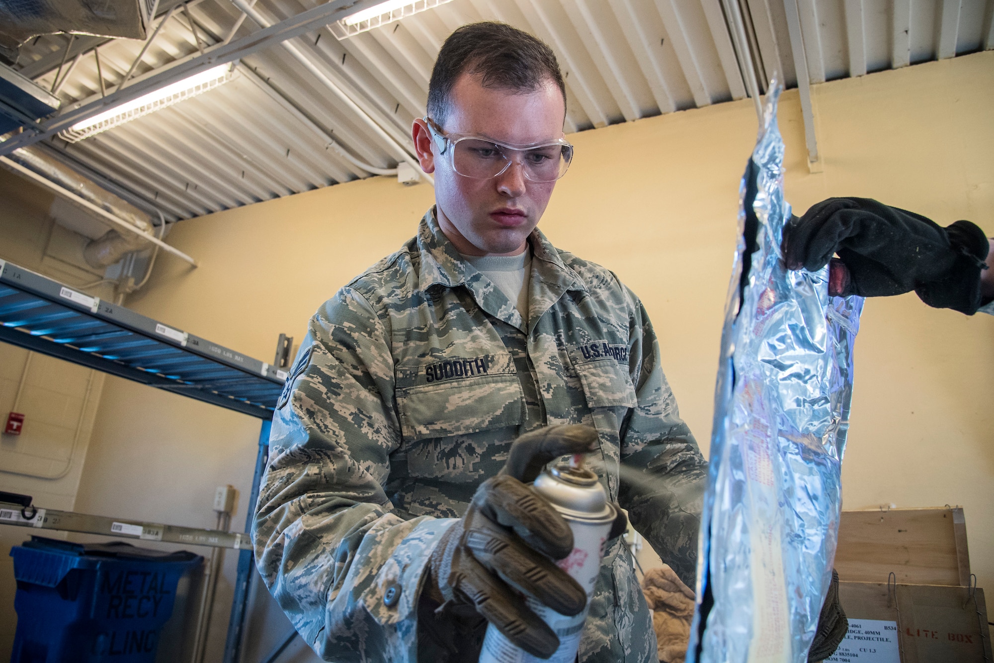 Senior Airman William Suddith, 23d Maintenance Squadron (MXS) munitions inspector, sprays adhesive on packaging paper, July 10, 2018, at Moody Air Force Base, Ga. Munitions inspectors from the 23d MXS are responsible for the meticulous inspection, packaging, and upkeep procedures for a stockpile valued at 54 million dollars, they enhance Moody’s combat capabilities by providing safe and serviceable ammo. (U.S. Air Force photo by Airman 1st Class Eugene Oliver)