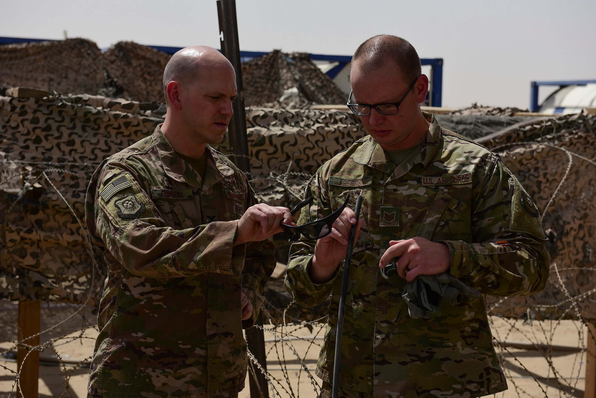 Two Airmen look at a small wire