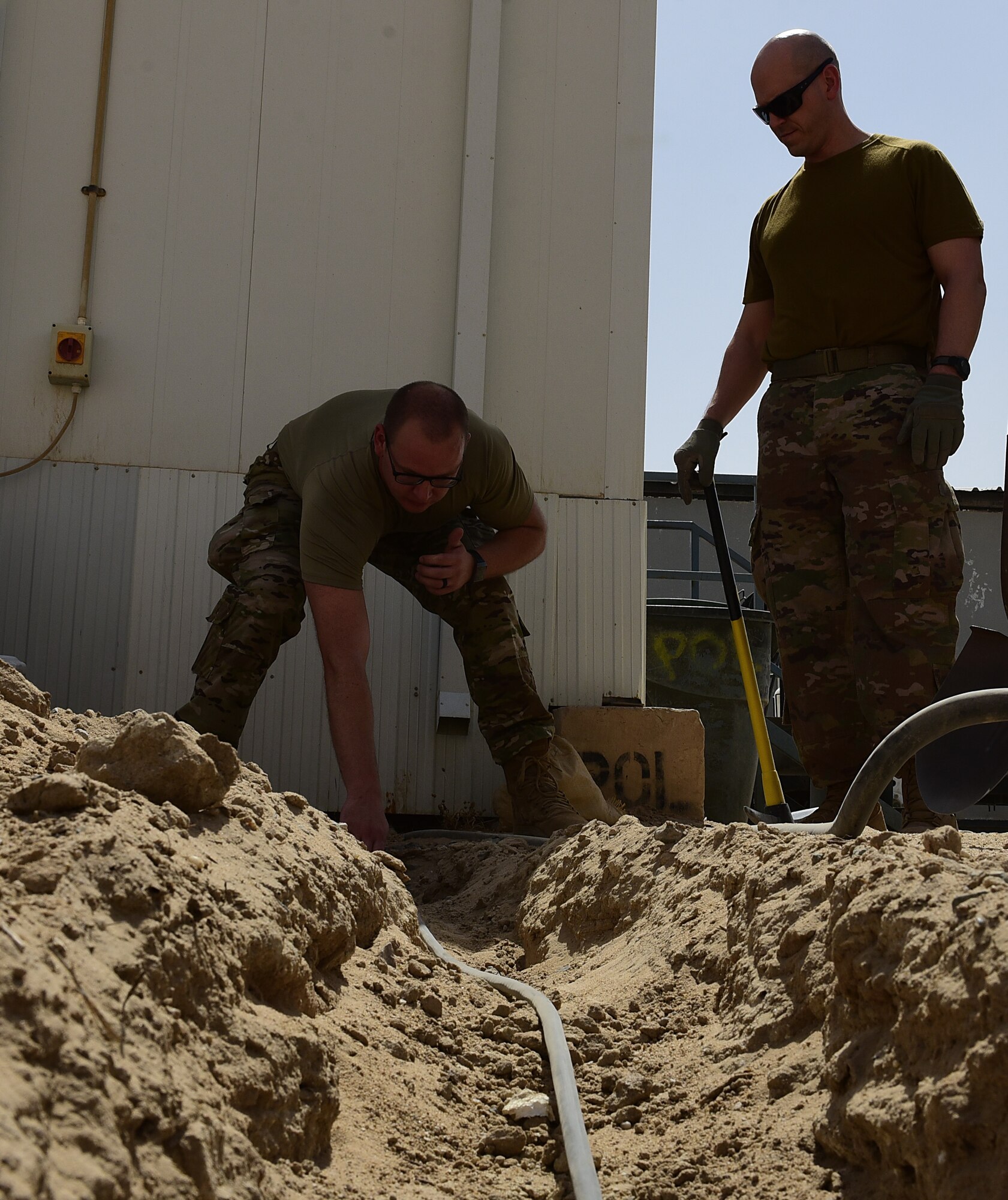 Two Airman place a cable in a hole in the ground