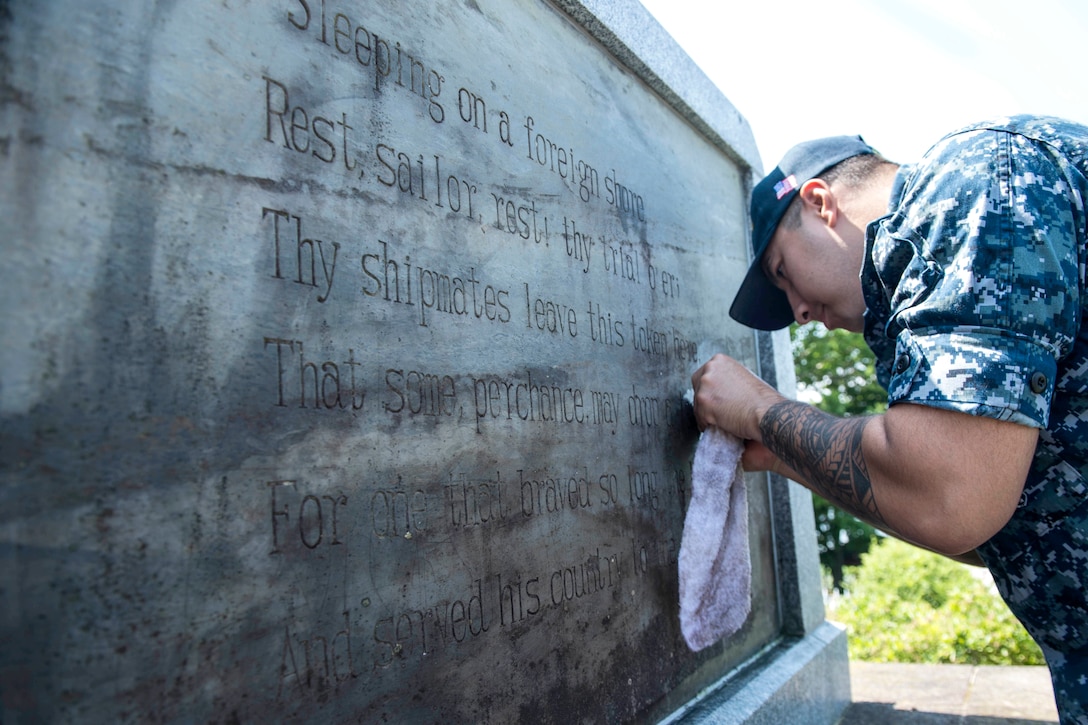 A sailor uses a towel to clean a memorial