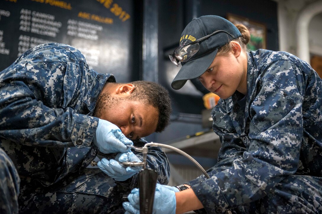Two sailors sit on the ground performing maintenance.