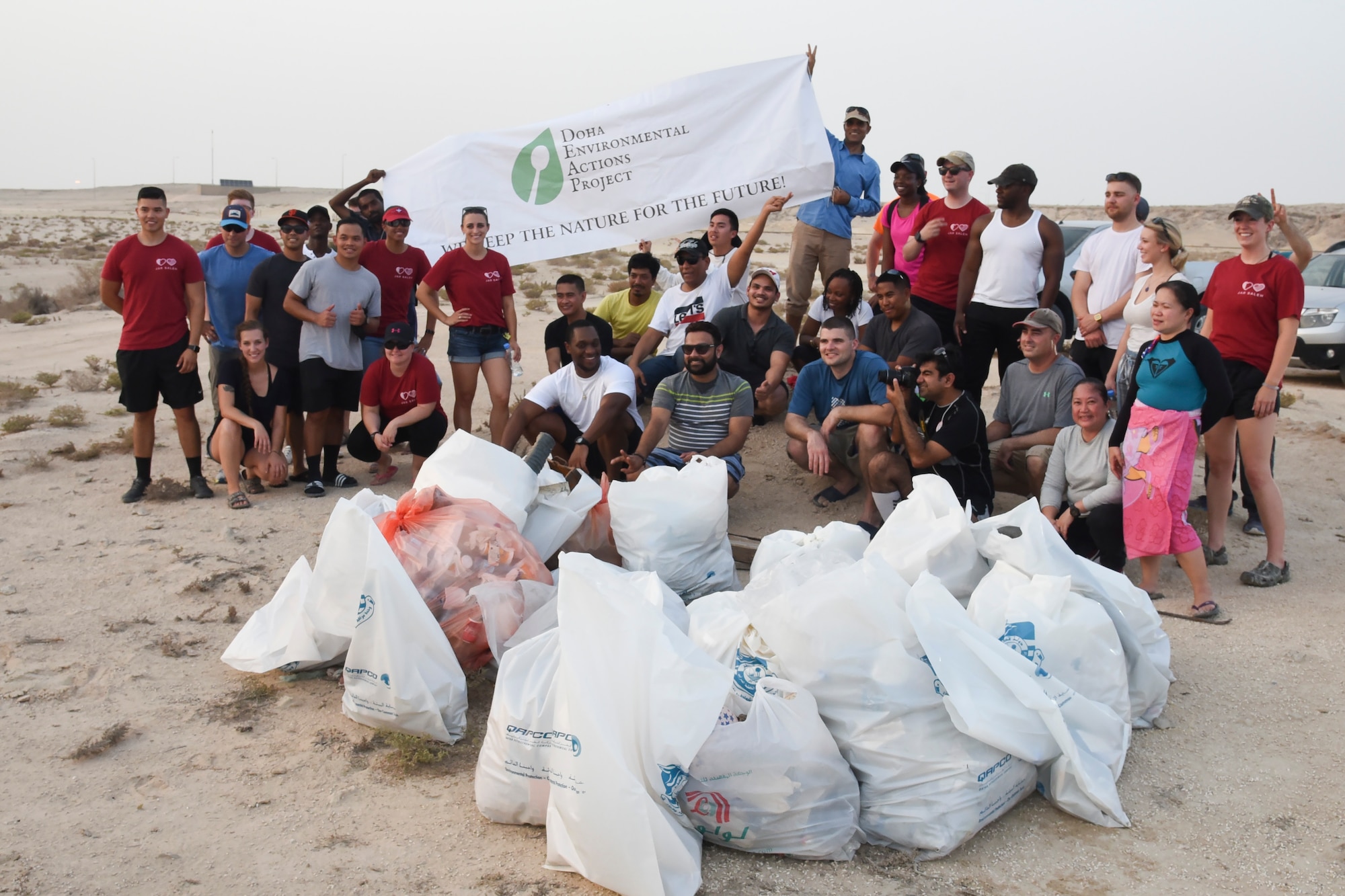 Members of Jar Saleh, a volunteer organization at Al Udeid Air Base, pose with members of members of the Doha Environmental Actions Project after gathering more than ten bags of trash during a beach cleanup event in Doha, Qatar, July 6, 2018. Jar Saleh works alongside the host nation’s community groups to continue a good-faith relationship through acts of kindness and generosity. (U.S. Air Force photo by Staff Sgt. Enjoli Saunders)