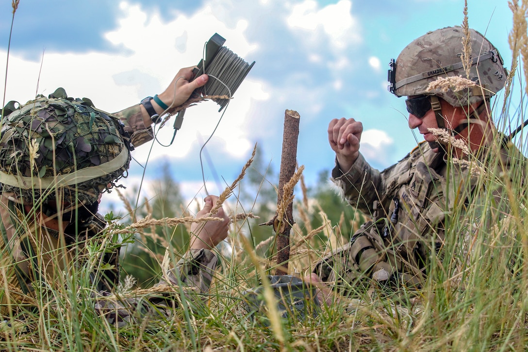 A U.S. and British soldier attach the detonation cord to an M18A1 Claymore mine.