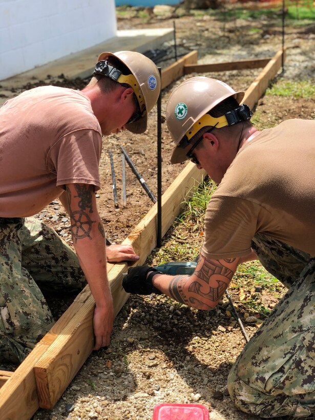 Two sailors work together to install wood formwork for a sidewalk.