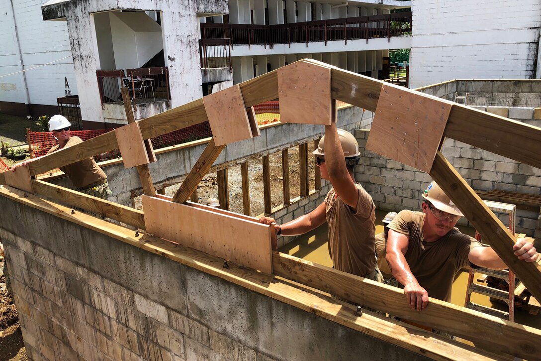 Navy sailors work together to install roof trusses on the work site.