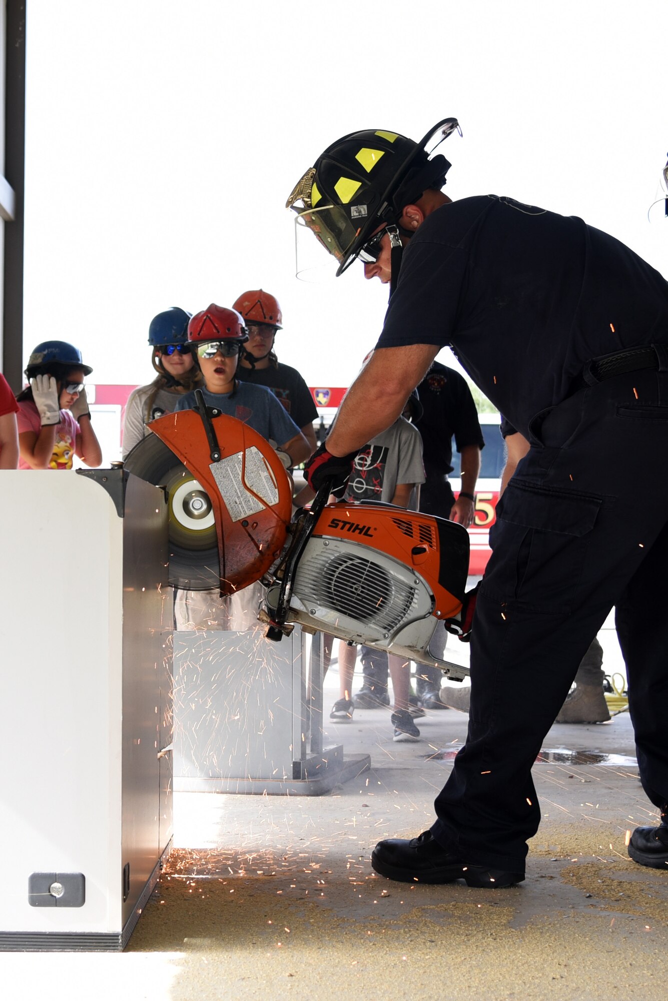 17th Civil Engineer Squadron hazardous material and emergency medical technician, Bradley Keibler, cuts through a desk during a Junior Firefighter Camp demonstration at the Fire Station on Goodfellow Air Force Base, Texas, July 17, 2018. During the Junior Firefighter Camp, the children learned how to use fire extinguishers, tie a variety of knots and how to safely climb and descend a ladder. (U.S. Air Force photo by Staff Sgt. Joshua Edwards/Released)