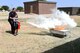 17th Civil Engineer Squadron fire inspector, Billy Clemons, assist junior firefighter, Elijah Scott, with a fire extinguisher during the Junior Firefighter Camp at the Fire Station on Goodfellow Air Force Base, Texas, July 18, 2018. Scott and other junior firefighters learned how to use different extinguishers for different types of fire. (U.S. Air Force photo by Staff Sgt. Joshua Edwards/Released)