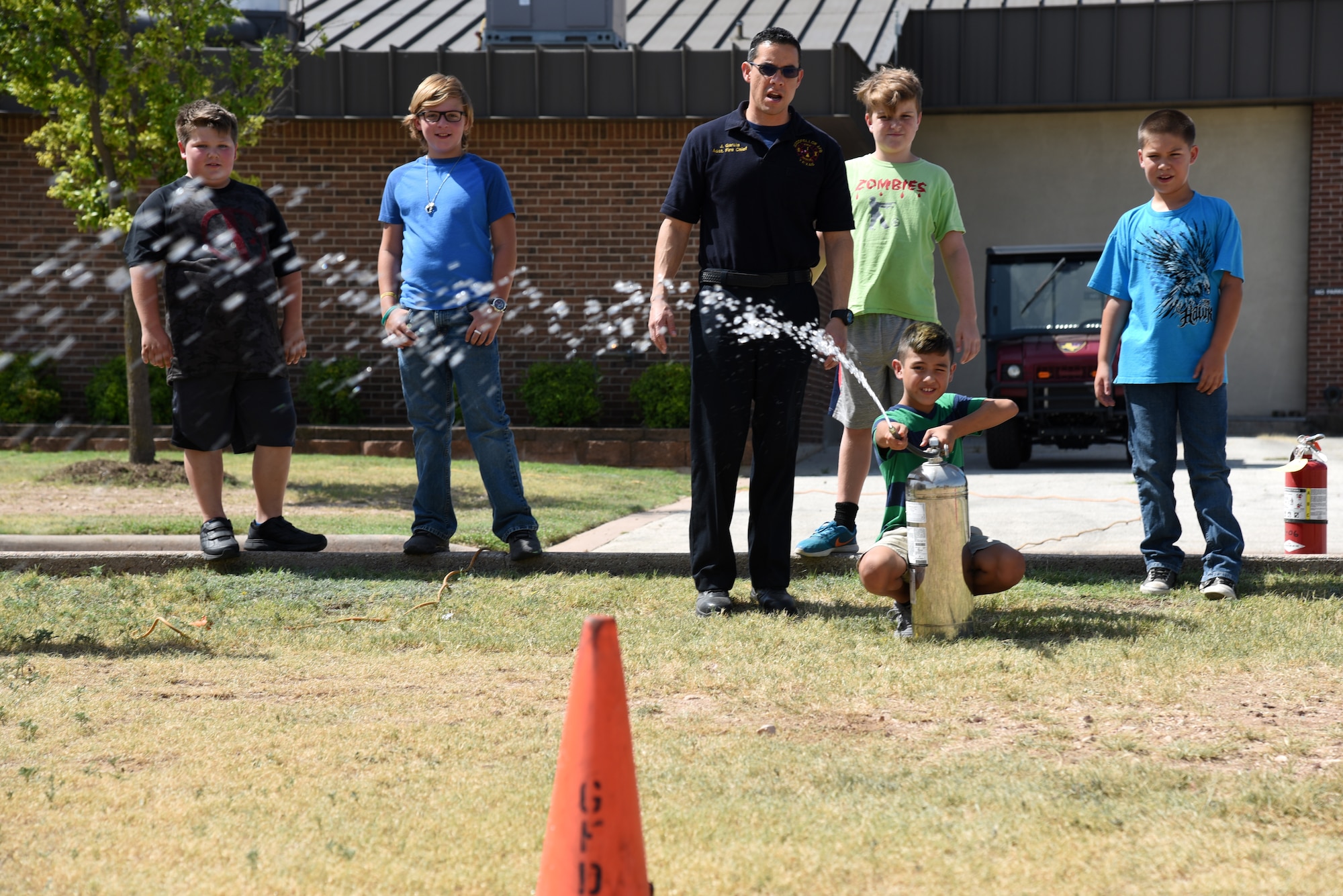 Junior firefighter, Canon DeAnda, sprays a fire extinguisher towards a cone during the Junior Firefighter Camp at the Fire Station on Goodfellow Air Force Base, Texas, July 18, 2018. DeAnda also practiced fighting a fire with a different type extinguisher. (U.S. Air Force photo by Staff Sgt. Joshua Edwards/Released)