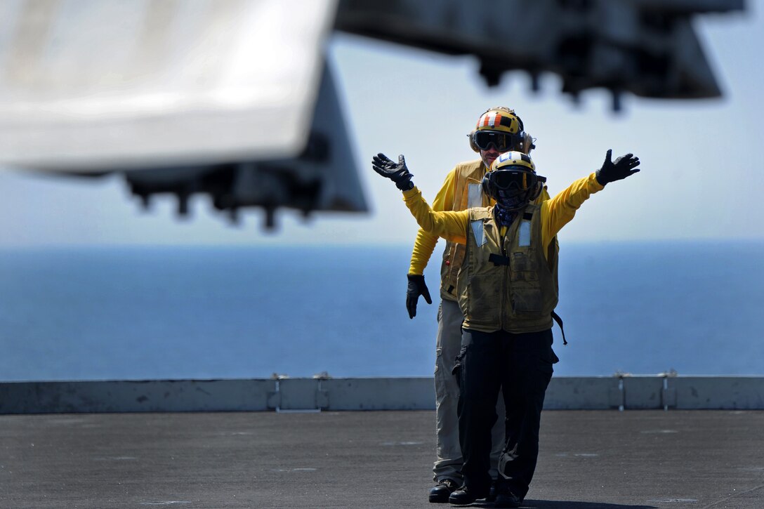 Sailors use hand signals to direct an F/A-18 Super Hornet.