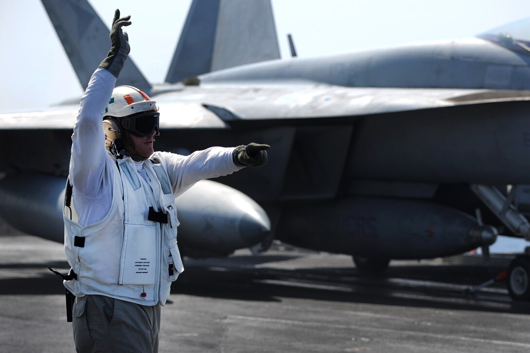 A sailor uses hand signals while preparing to launch an aircraft.