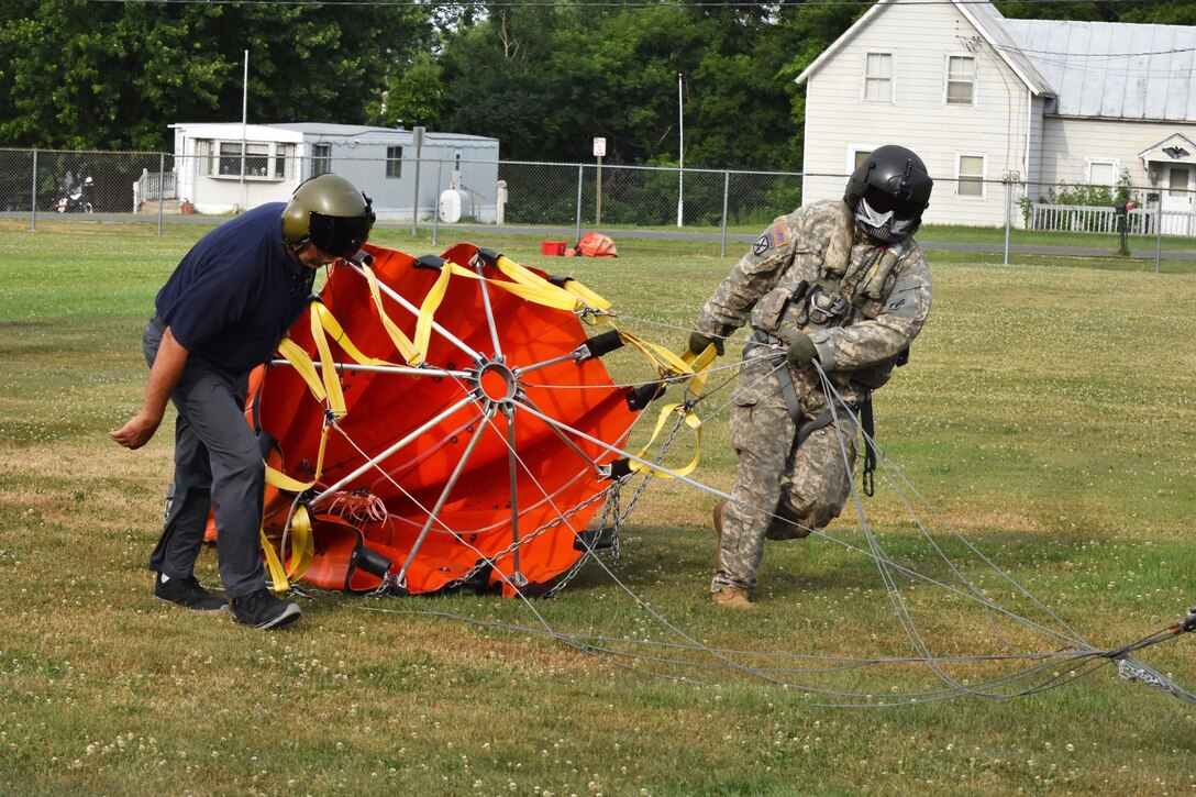 A soldier and civilian drag a bucket firefighting system.