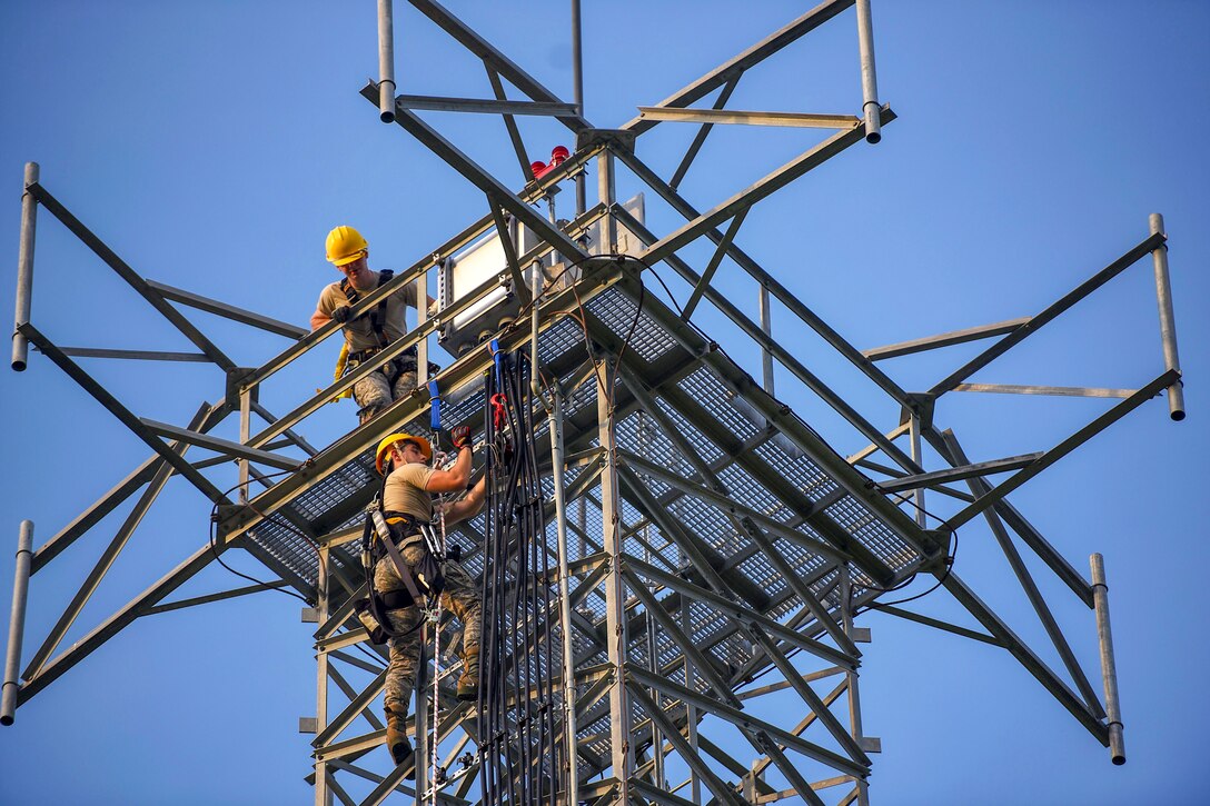 Airmen in yellow hard hats work atop a tower.