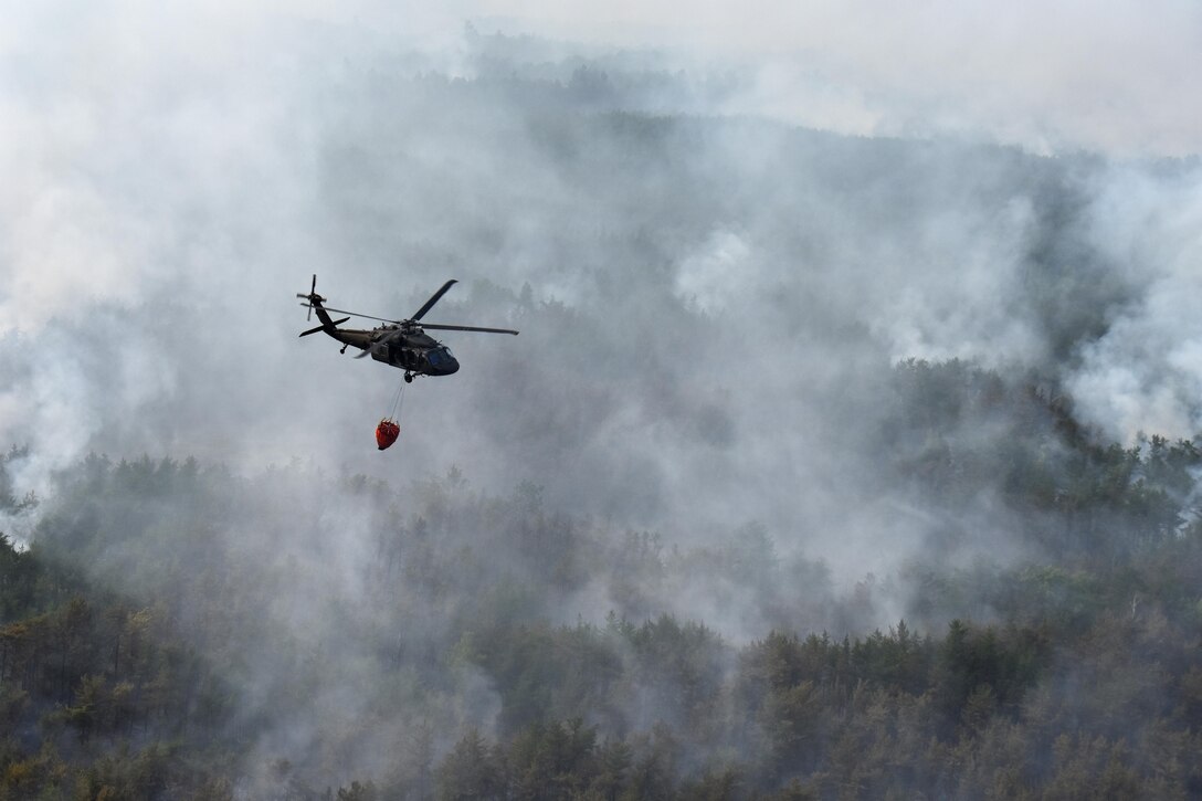 A UH-60 Black Hawk helicopter crew flies over a forest fire.
