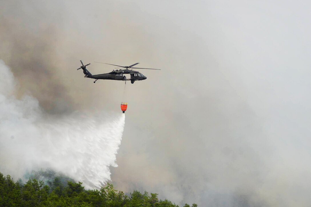 A helicopter releases water from a bucket firefighting system while on a firefighting mission.