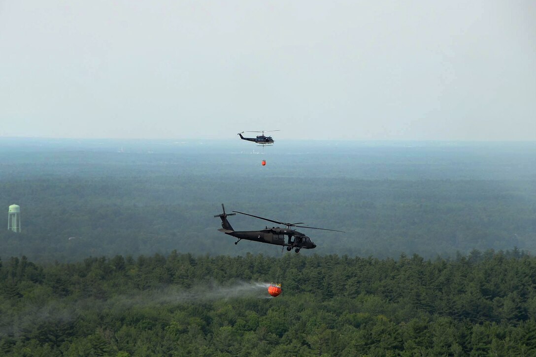 Two helicopters release water from their bucket firefighting systems while on a firefighting mission.