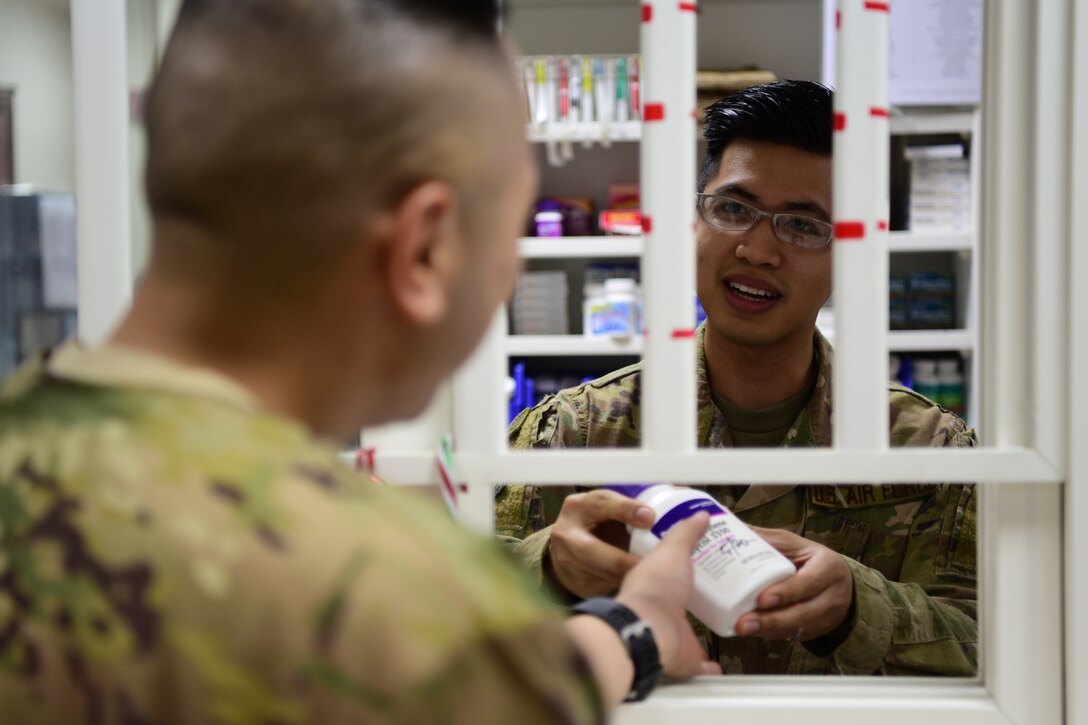 An airman gives a bottle of medication to a coworker.