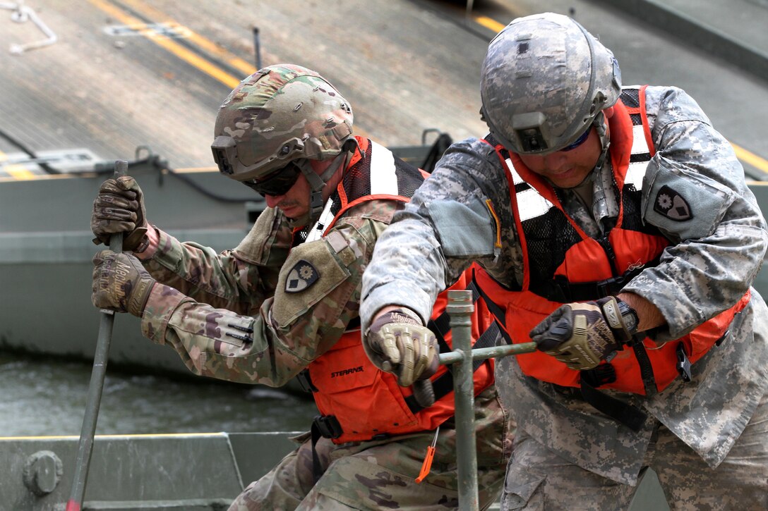 Soldiers use bridging tools to dismantle a 100-foot temporary floating bridge.