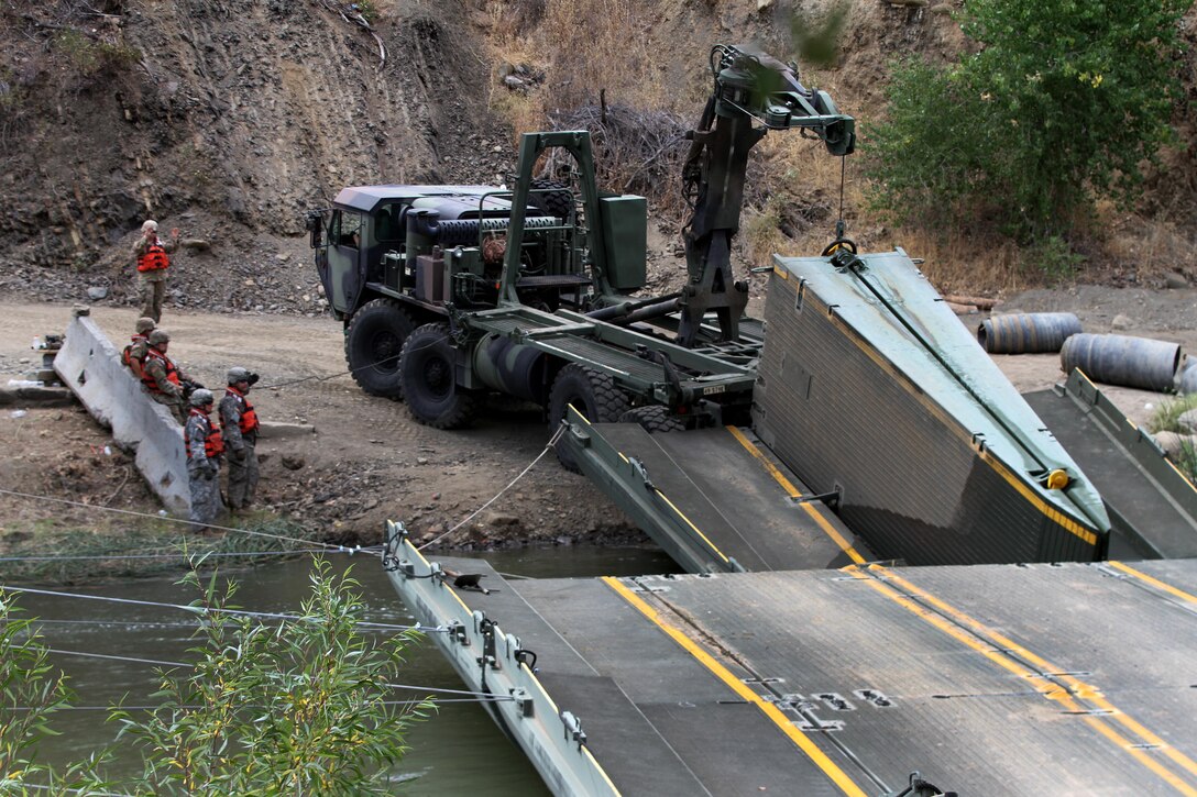 Soldiers use heavy equipment to dismantle a 100-foot temporary floating bridge.