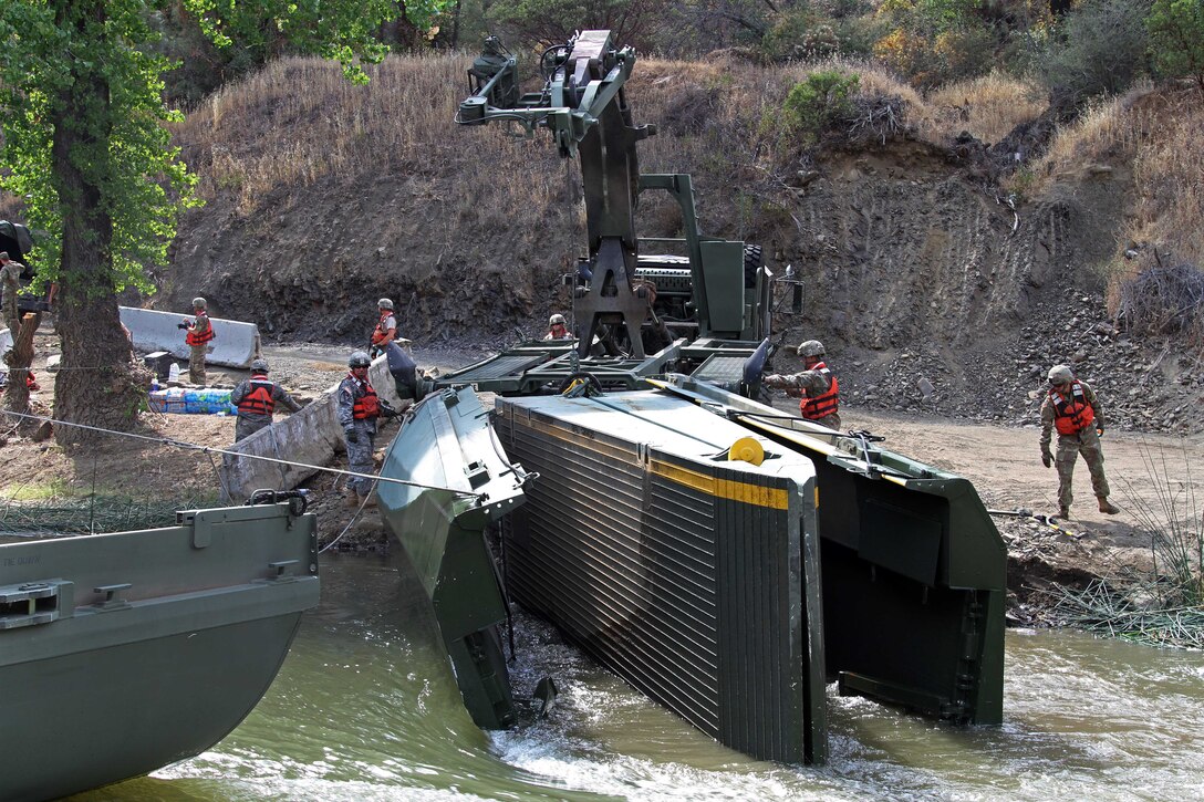 Soldiers operate heavy equipment to pull a portion of a dismantle 100-foot temporary floating bridge.