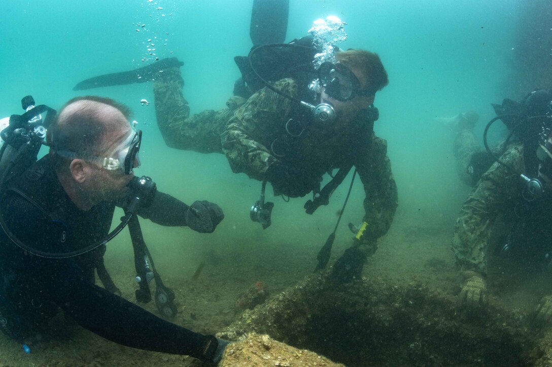 Navy divers search the ocean floor while conducting a training dive mission.