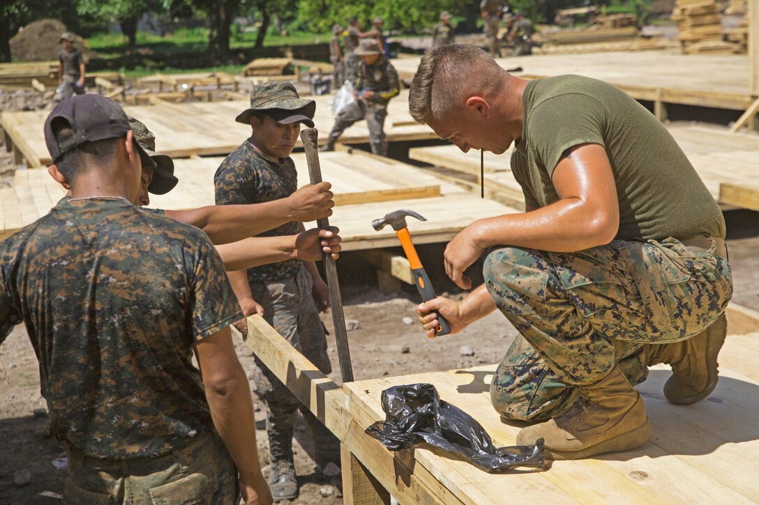 A Marine uses a hammer to help several other troops build a shelter.