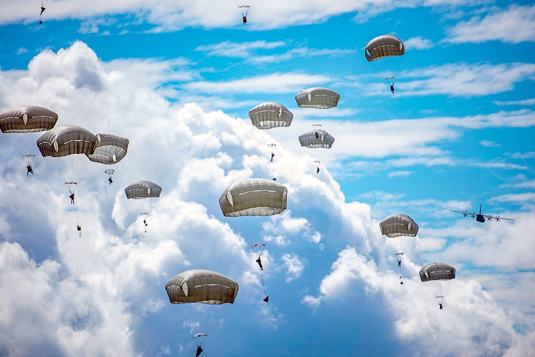Soldiers drift down on parachutes in the sky.