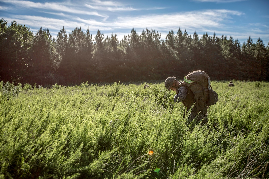 A Marine walks through a field carrying a pack.
